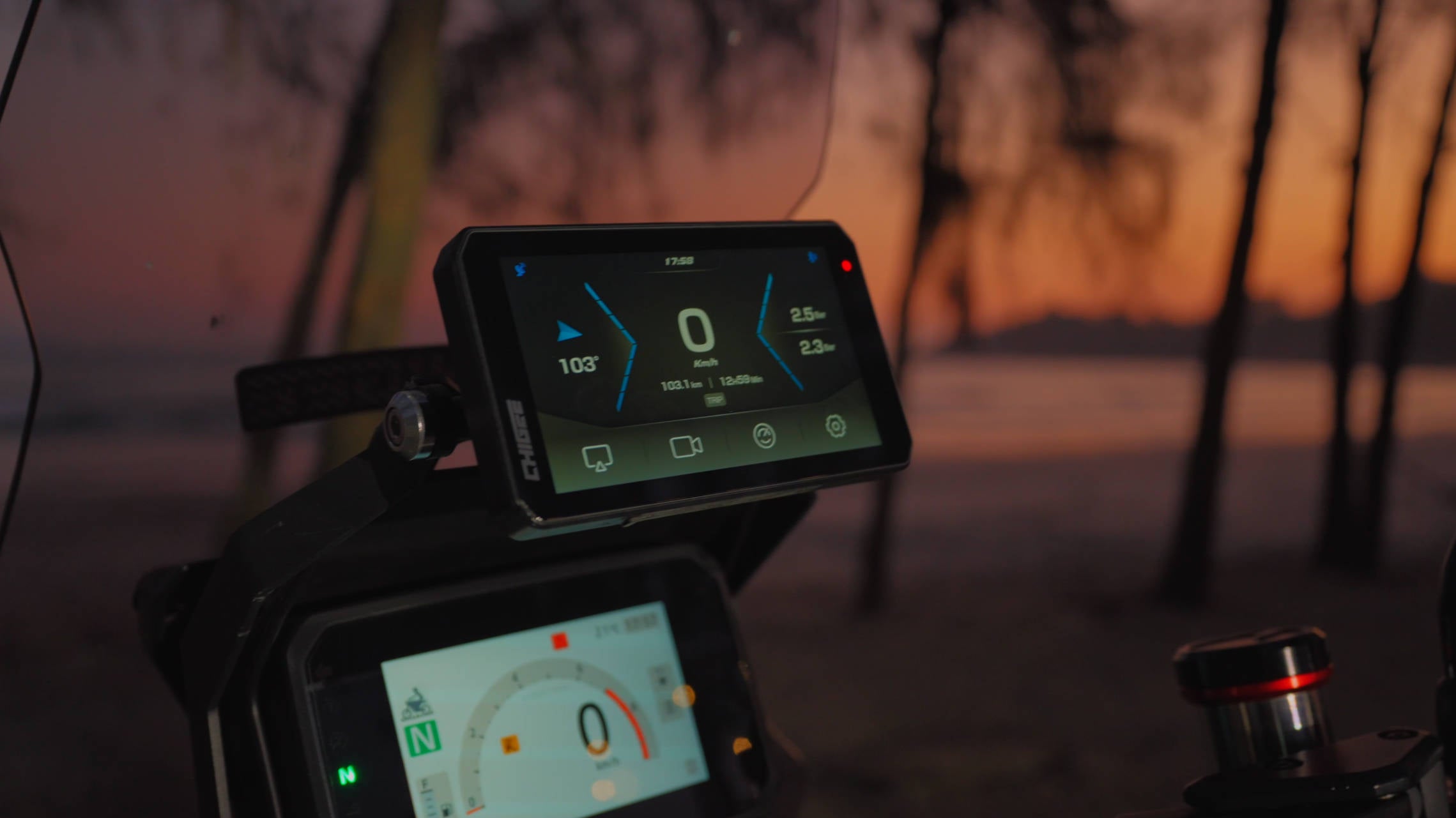 Close-up of a AIO-5 EVOdigital display on a vehicle with a sunset or sunrise background.